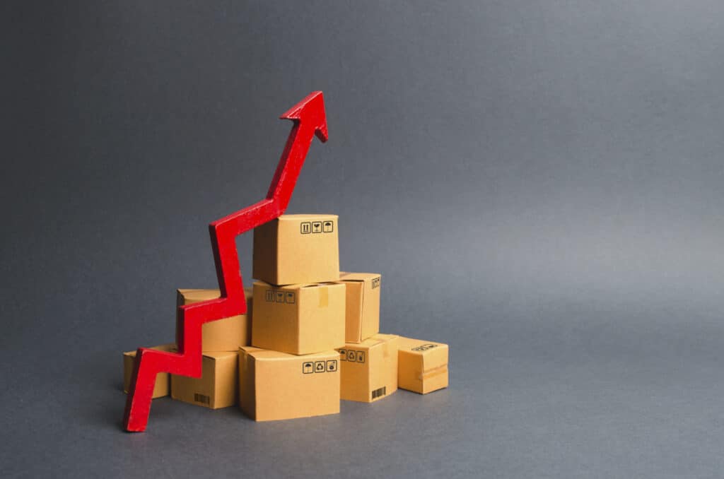 A pile of cardboard boxes and a green up arrow. The growth rate of production of goods and products, increasing economic indicators. Increasing consumer demand, increasing exports, imports. sales rise