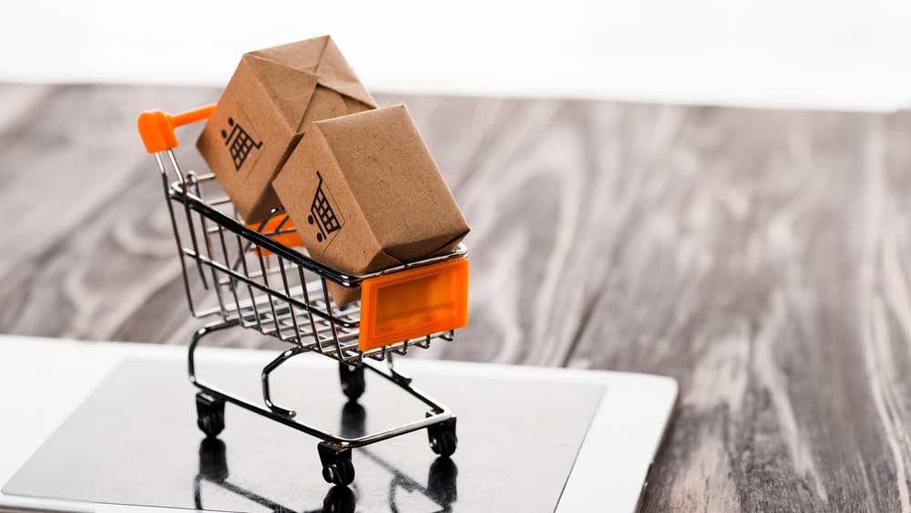 A miniature shopping cart on a laptop keyboard filled with small cardboard boxes, symbolizing online shopping and the convenience of e-commerce.