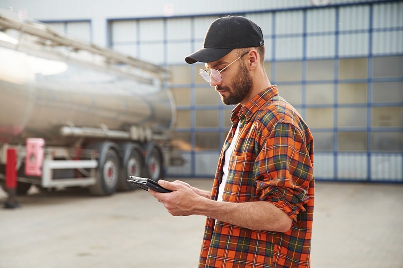 Truck driver stands in front of his rig, reviewing data on his phone.