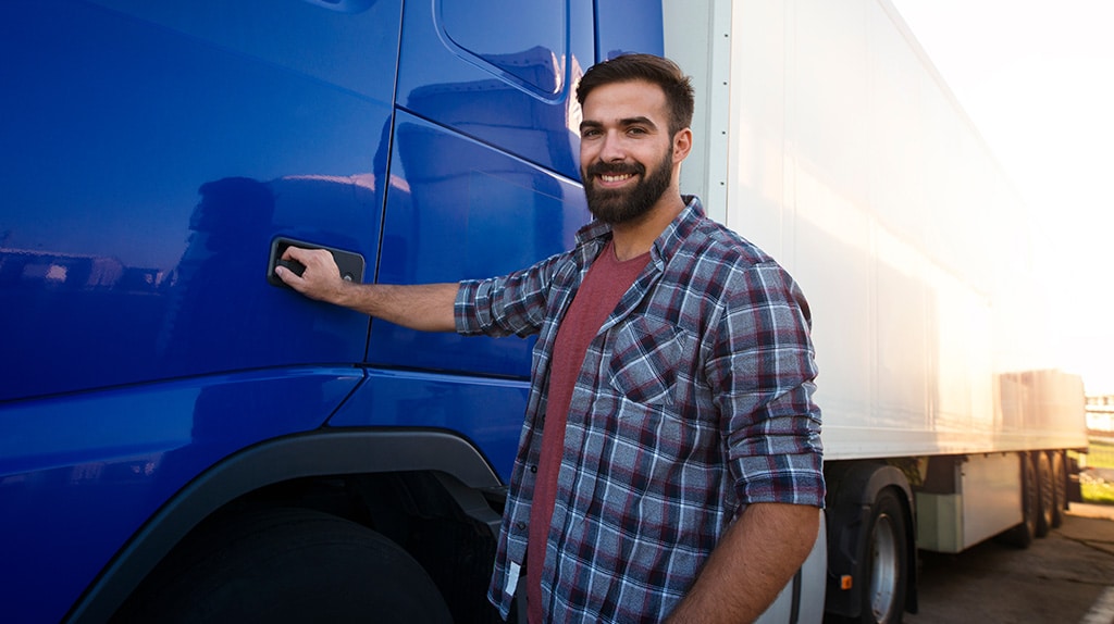 Young truck driver smiles while holding cab door to his semi truck. 